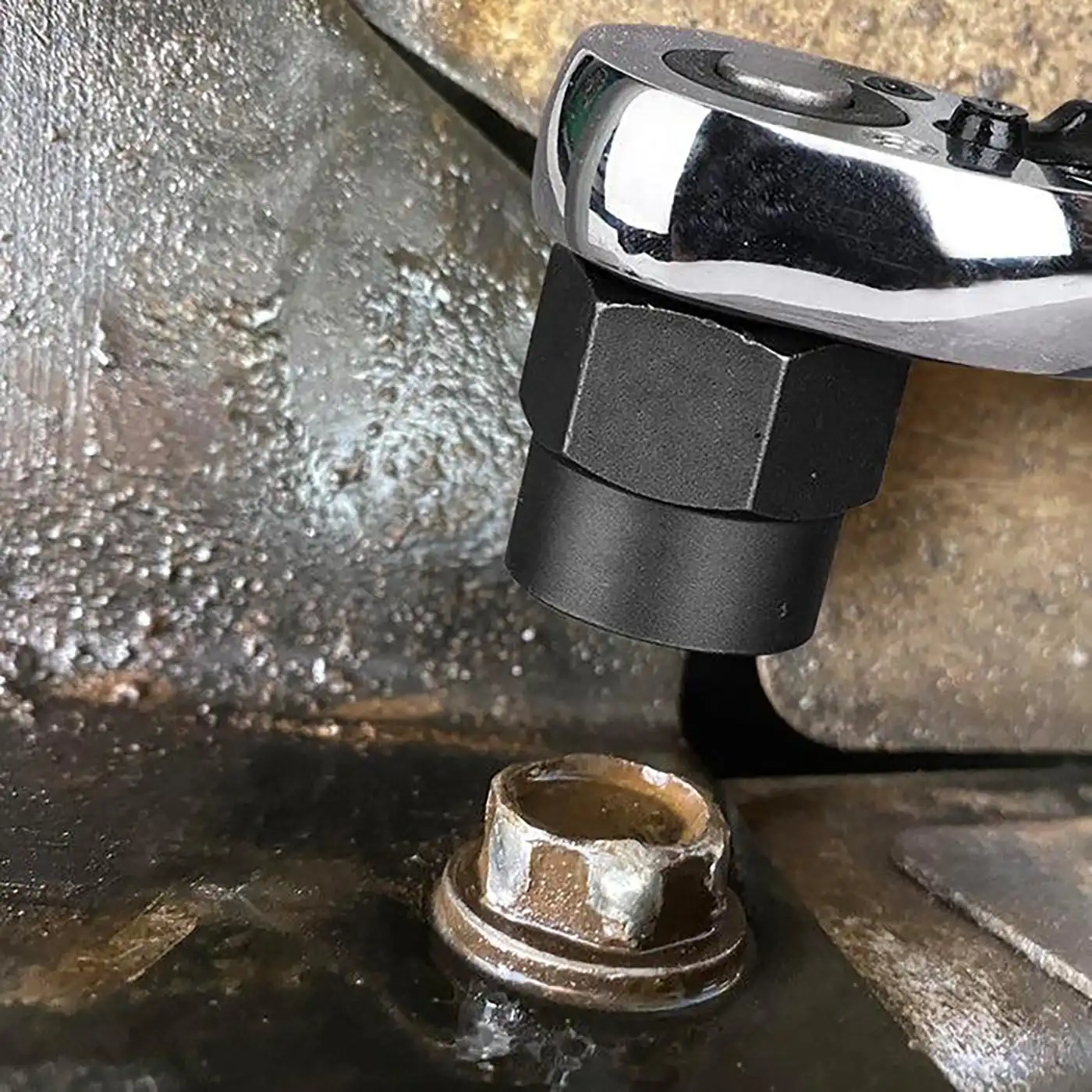 A socket on a ratchet held above a corroded hex-head bolt whose corners are visibly rounded and chipped.